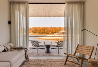 Salotto moderno e luminoso in una Waterlodge al Resort de Parel, Paesi Bassi, con vista lago e bosco autunnale.