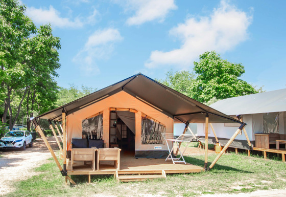 Safaritent Comfort + airco, modern safari tent with deck, outdoor seating and view of trees and sky.
