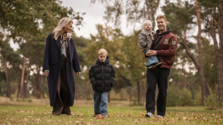Een familie wandelt samen door het gras nabij Holiday villa Amalia 6, omgeven door bos en natuur.