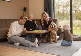 Familia se divierte jugando a un juego de mesa y con su perro en Holiday villa Amalia 6, Hofparken De Bergvennen.
