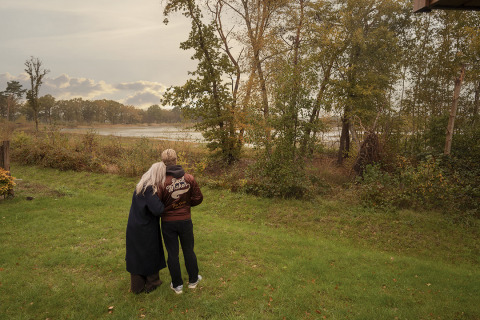Twee mensen staan samen op het gras bij een lodge en kijken uit over het landschap.