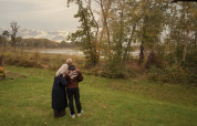 Two people stand close together on a grassy lawn at a lodge, looking out over the scenic landscape.