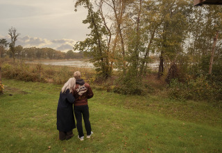 Twee mensen staan samen op het gras bij een lodge en kijken uit over het landschap.