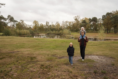 Family walks in grassy park near pond at Vacation villa Amalia 4 with hot tub at Hofparken De Bergvennen.