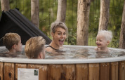 En familie hygger sig sammen i en udendørs træ-vildmarksbad på en lodge omgivet af natur og træer.