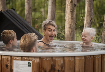 Een vrolijk gezin ontspant samen in een houten buitenjacuzzi bij een lodge midden in de natuur.