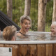 Eine fröhliche Familie genießt gemeinsam ein warmes Holzbad im Freien an einer naturreichen Lodge.