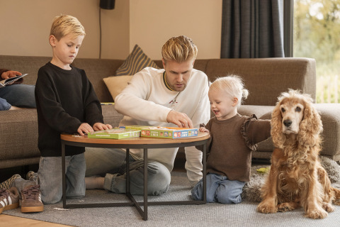 Familie leger brætspil med børn og hund i stue i Vacation villa Amalia 4 hos Hofparken De Bergvennen.