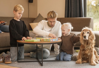Gezin speelt een bordspel met kinderen en hond in de woonkamer van Vacation villa Amalia 4 in Nederland.