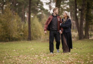 A smiling couple walks hand in hand in a green park at Holiday Villa Amalia 2 + sauna at Hofparken De Bergvennen.