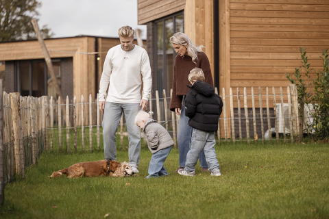 Een gezin met twee kinderen en een hond amuseert zich bij een lodge in Hofparken De Bergvennen, Nederland.