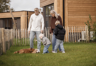 Een gezin met twee kinderen en een hond amuseert zich bij een lodge in Hofparken De Bergvennen, Nederland.
