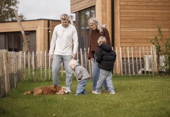 Une famille avec deux enfants et un chien profite du jardin devant leur lodge à Hofparken De Bergvennen.