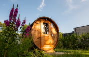 Barrel-shaped wooden sauna at Holiday villa Amalia 2, surrounded by flowers and greenery at Hofparken Wiltershaar.