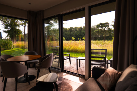 Sunny lodge interior with comfortable seating, open patio doors, and view of meadow and trees outside.