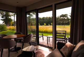 Sunny lodge interior with comfortable seating, open patio doors, and view of meadow and trees outside.