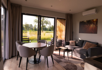 Moderne stue i ferievilla Amalia 2 med spisebord, sofa og udsigt mod natur ved Hofparken Wiltershaar, NL.