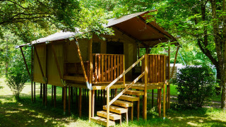 Tienda safari llamada Safaritent 4 para 4 personas, elevada sobre pilotes y rodeada de árboles verdes.