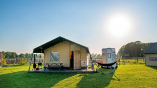 Safari-Zelt Luxe Ranchtent auf einer sonnigen Wiese mit Hängematte, Holztisch und Grill im Freien.