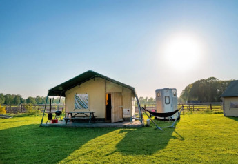 Safari-Zelt Luxe Ranchtent auf einer sonnigen Wiese mit Hängematte, Holztisch und Grill im Freien.