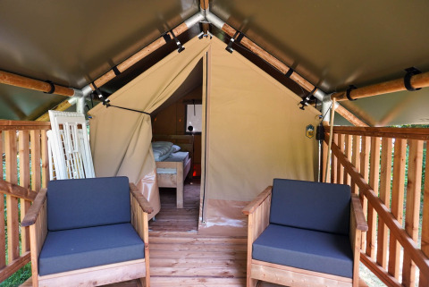 Entrance of safari tent with wooden veranda and chairs at Camping De Rammelbeek, Netherlands, bed inside visible.
