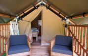 Eingang zu einem Safarizelt mit Holzveranda und Stühlen auf Camping De Rammelbeek, Niederlande, Bett sichtbar.