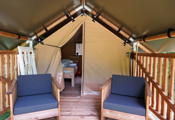 Eingang zu einem Safarizelt mit Holzveranda und Stühlen auf Camping De Rammelbeek, Niederlande, Bett sichtbar.
