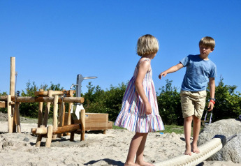 Deux enfants jouent pieds nus sur une aire de jeux en sable à un hébergement de glamping en plein air.