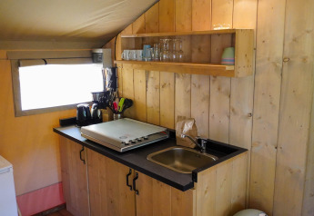 Petite kitchenette dans une tente safari avec évier, plaque de cuisson, ustensiles et étagères ouvertes.