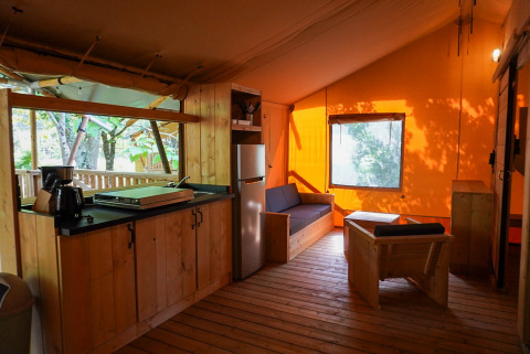 Interior de una tienda safari para 6 personas con cocina, zona de estar y baño privado junto al lago.