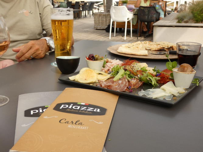 Comida al aire libre en glamping con antipasto italiano, bebidas y cartas sobre la mesa en ambiente relajado.