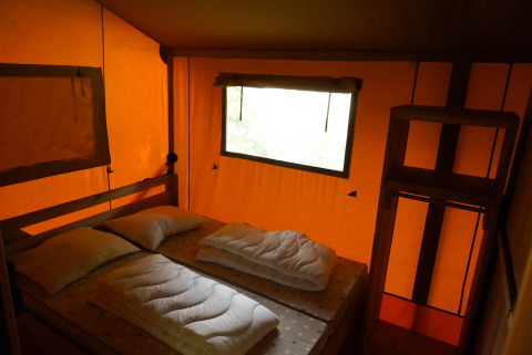 Innenansicht eines Safarizeltes mit Doppelbett, Kopfkissen und Fenster am Camping De Rammelbeek, Niederlande.