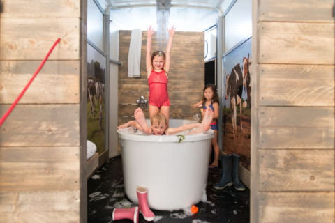 Bambini che giocano nella vasca da bagno nella tenda safari Luxe Ranchtent, con pareti in legno e mucche.