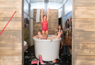 Bambini che giocano nella vasca da bagno nella tenda safari Luxe Ranchtent, con pareti in legno e mucche.