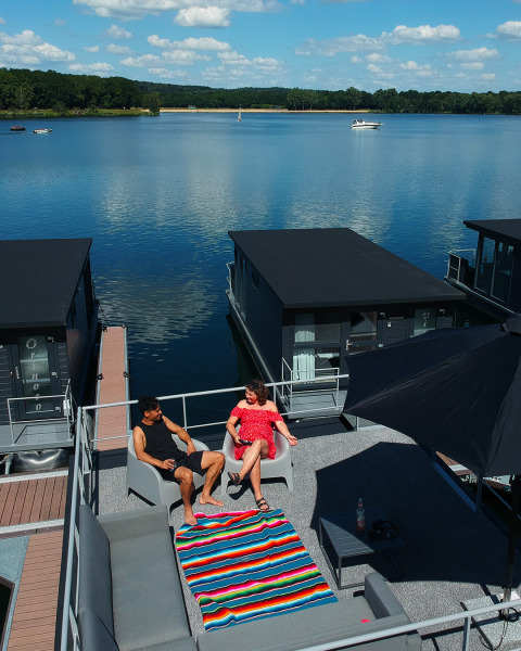 A couple relaxes on a roof terrace of a houseboat lodge at Marina Mookerplas in the Netherlands on a sunny day.