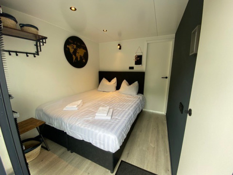 Chambre de glamping confortable avec lit double, linge blanc, déco murale et paniers de rangement.