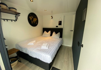 Camera glamping accogliente con letto matrimoniale, biancheria bianca, decorazioni e cesti portaoggetti.