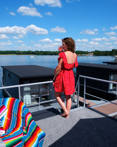Vrouw met rode jurk op het dakterras van een woonboot bij Marina Mookerplas in Nederland, genietend van het uitzicht.