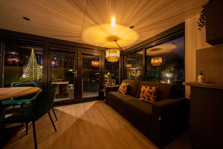 Gemütliches Wohnzimmer im Hausboot Marina Mookerplas in den Niederlanden mit Sofa und Blick auf Weihnachtsbaum.