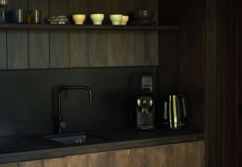 Donkere kitchenette in Nokken Forest Cabin met zwarte gootsteen, koffiezetapparaat, waterkoker en kopjes.