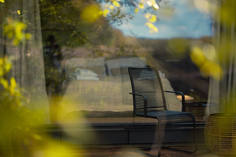 Moderner Stuhl vor Fenster der Nokken Forest Cabin bei Wilsumer Berge, Deutschland, mit Waldblick.