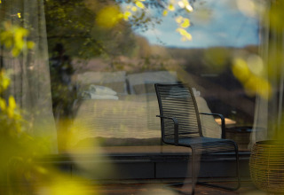 Moderne stol foran vinduet i Nokken Forest Cabin ved Wilsumer Berge, Tyskland, med udsigt til naturen.