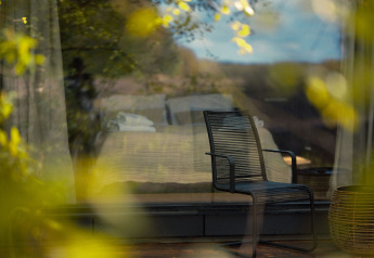 Chaise moderne devant la fenêtre de Nokken Forest Cabin à Wilsumer Berge, Allemagne, reflétant la nature.