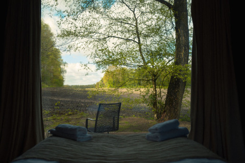 Vue depuis la Nokken Forest Cabin à Wilsumer Berge, Allemagne, lit avec serviettes et chaise dehors.