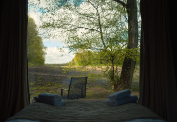 View from Nokken Forest Cabin at Wilsumer Berge in Germany, showing bed with towels and outdoor chair.