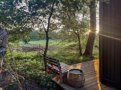 Zicht vanuit Nokken Forest Cabin in Wilsumer Berge, Duitsland, met houten terras en zonlicht door de bomen.