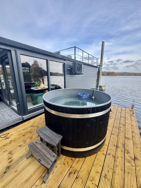 Outdoor hot tub on a wooden deck beside a modern houseboat at Marina Mookerplas, Netherlands, lakeside view.