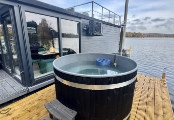 Buitenspa op houten terras naast een moderne woonboot aan Marina Mookerplas in Nederland met uitzicht op het meer.