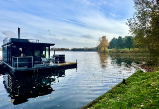 Houseboat with rooftop terrace and hot tub on a calm lake, surrounded by trees at Marina Mookerplas, Netherlands.