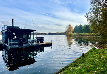 Woonboot met dakterras en hottub op een rustig meer, omgeven door bomen bij Marina Mookerplas, Nederland.
